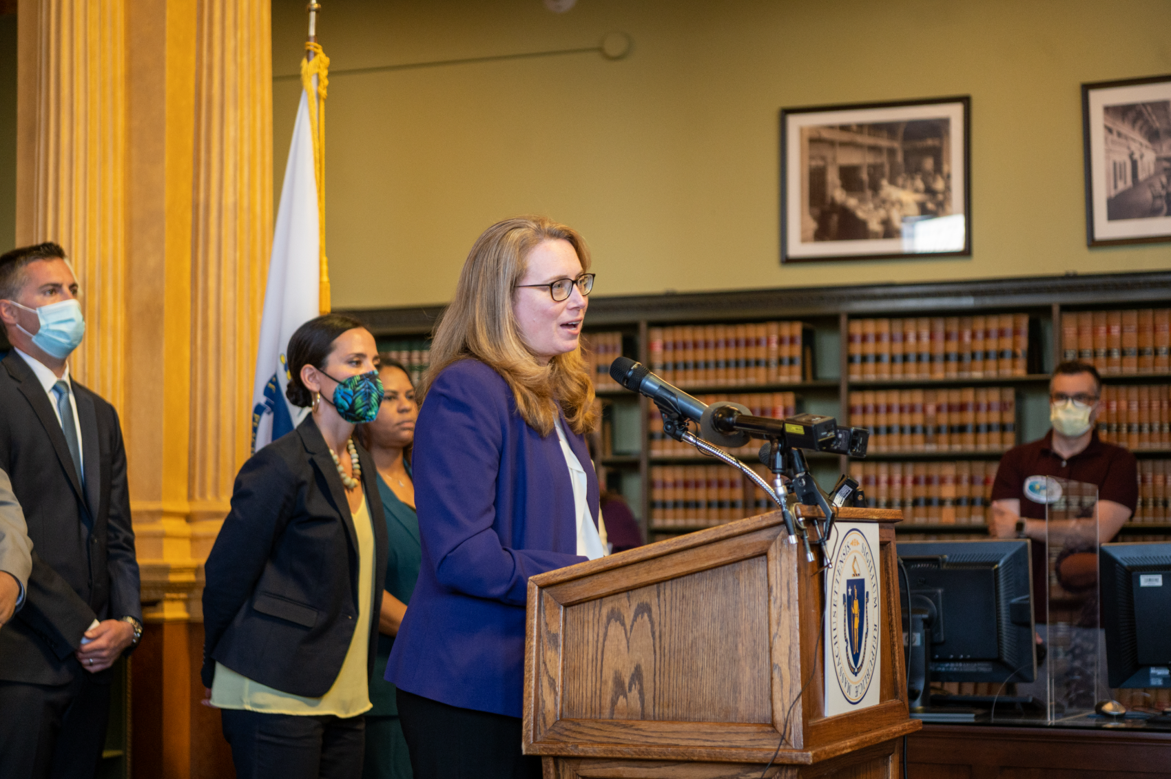 Christine Barber speaking at a State House podium, flanked by legislative colleagues